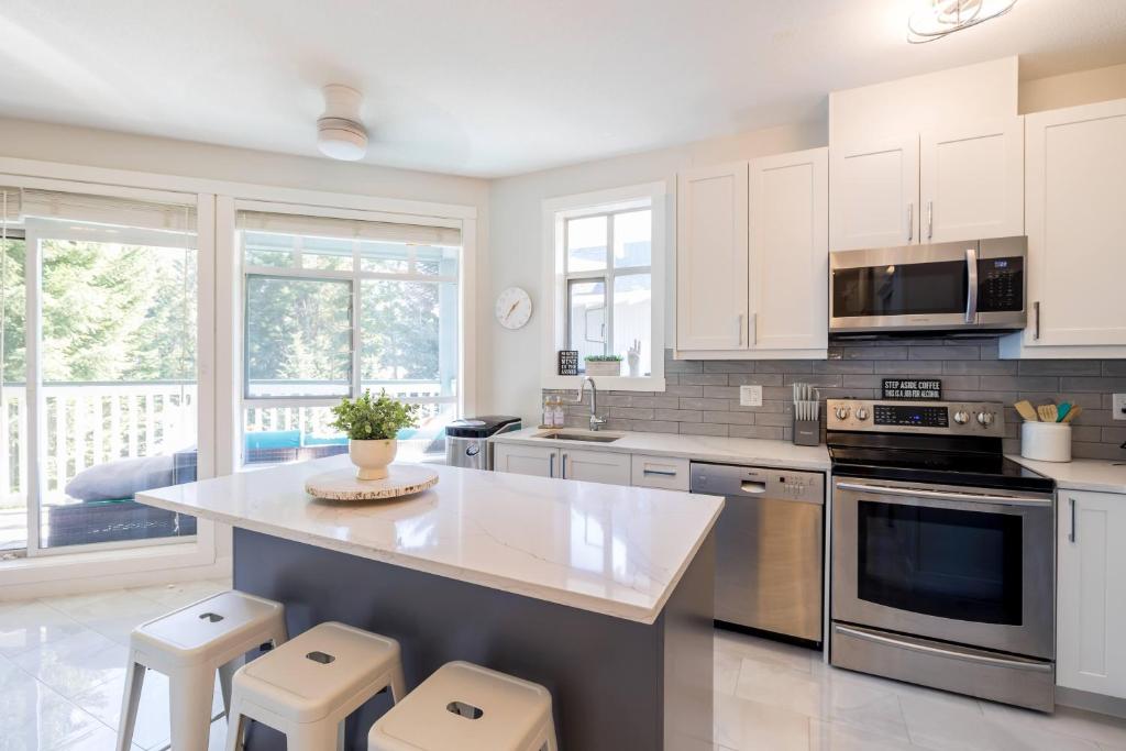Una cocina con gabinetes blancos y electrodomésticos de acero inoxidable. en Panoramic Views from this gorgeous 2 Bed Property - Village Location, en Whistler