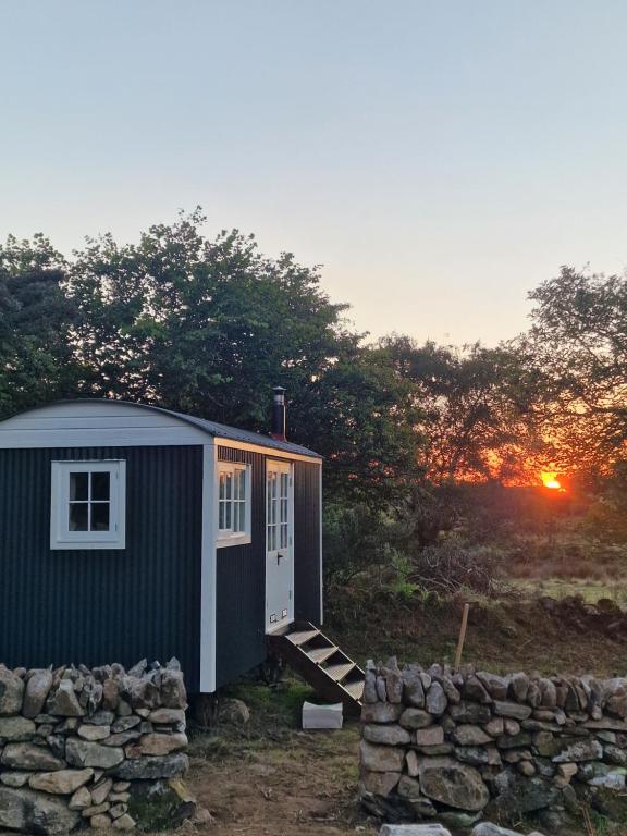 Una pequeña casa en un campo con la puesta de sol en el fondo en The Hazel Hut, en Westport