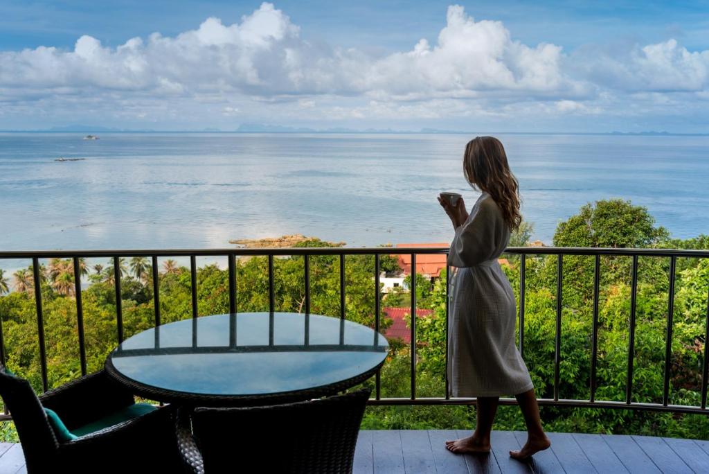 une femme debout sur un balcon donnant sur l'eau dans l'établissement Sunset Hill Boutique Resort Koh Phangan, à Haad Chao Phao