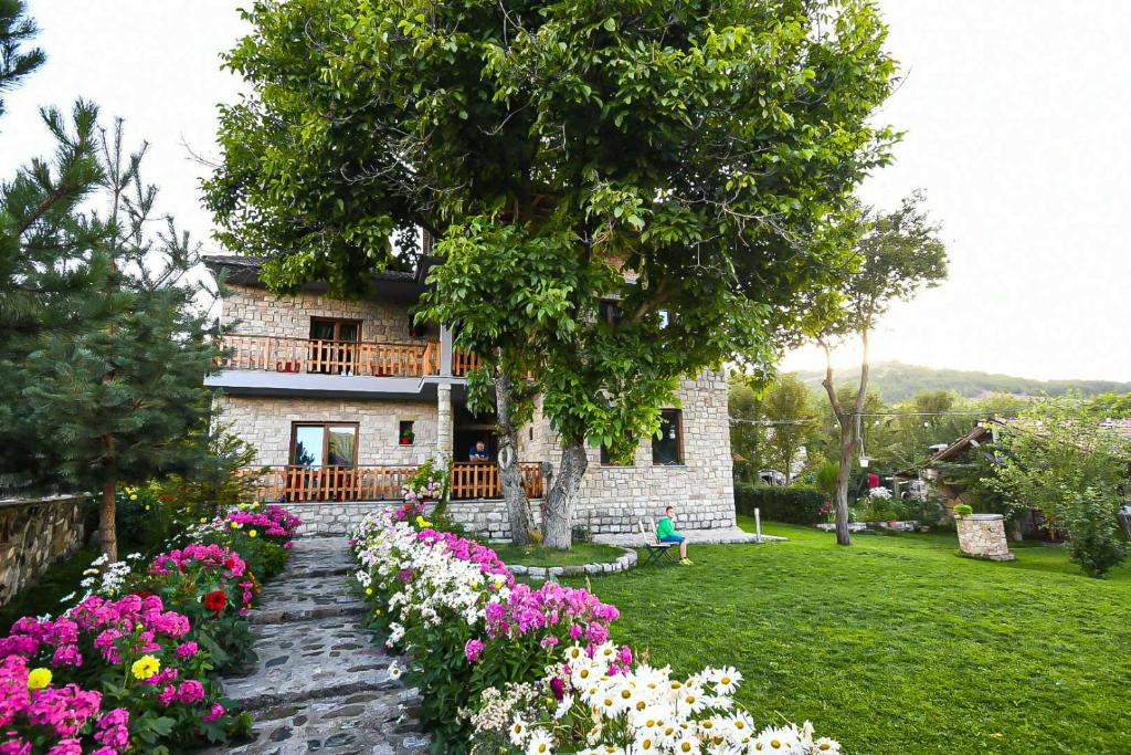 a stone house with flowers in the yard at Bujtina SHKODRANI in Voskopojë