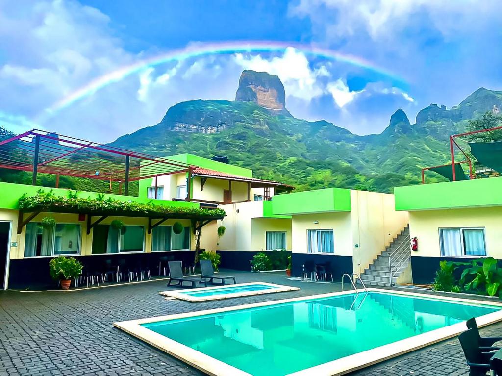 un arco iris sobre un hotel con piscina y montañas en Hotel São Jorge village en Órgãos