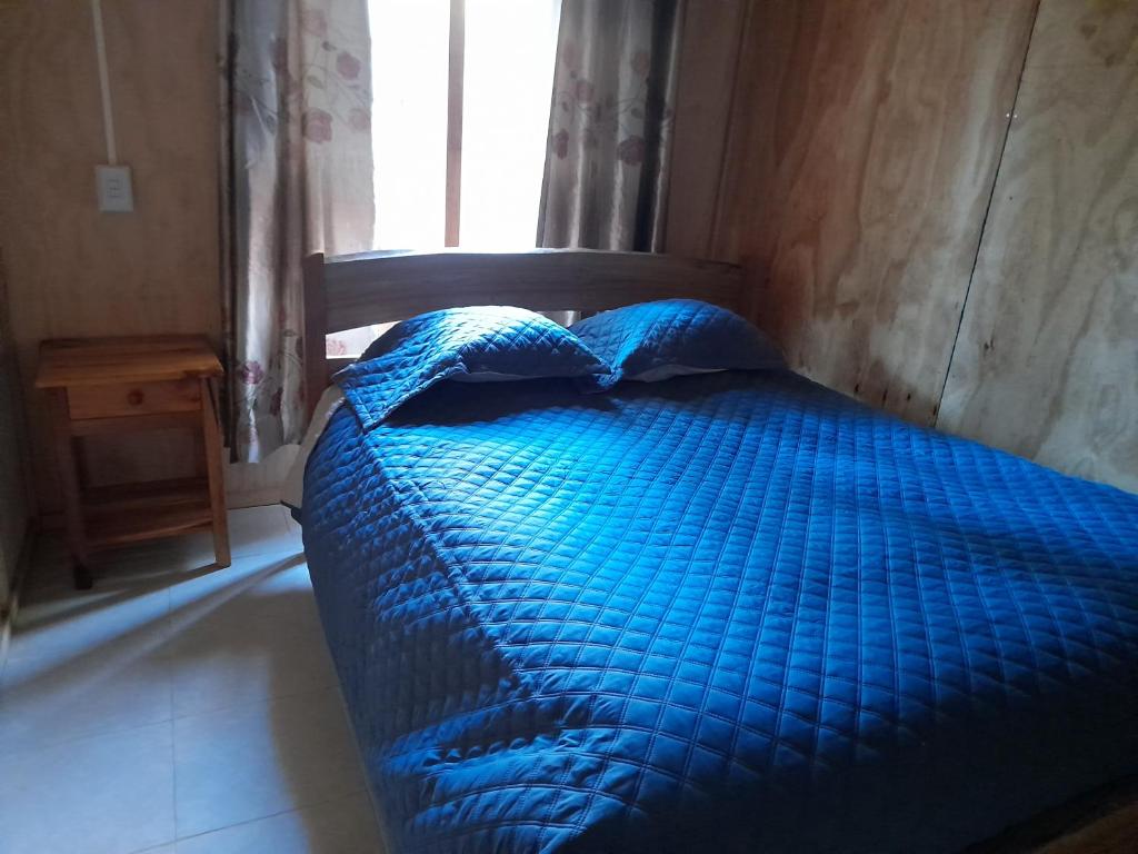 a blue bed in a room with a window at Cabañas Nehuen Coyan in Melipeuco