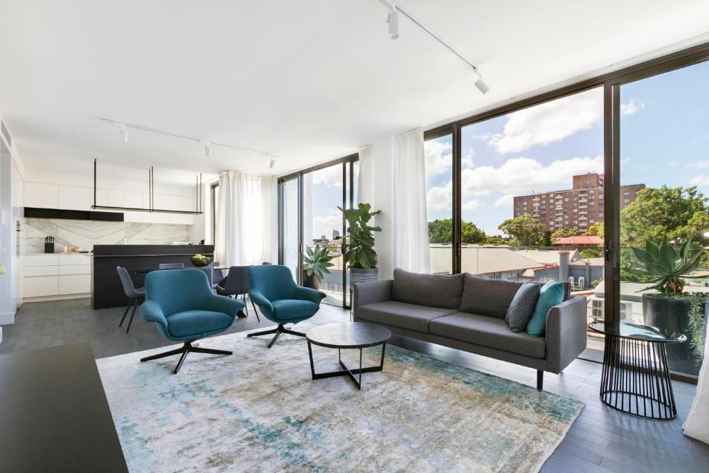 een woonkamer met een bank, stoelen en ramen bij Botanik Apartment Hotel in Sydney