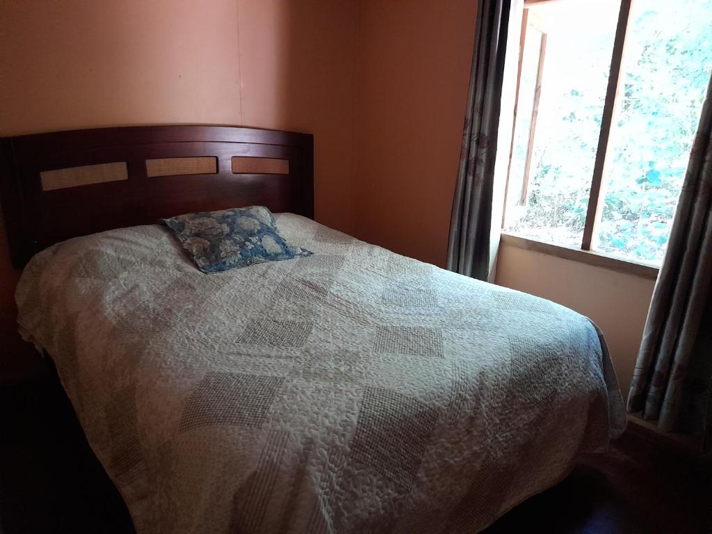 a bed with a quilt on it in a room with a window at Refugio de montaña in Melipeuco