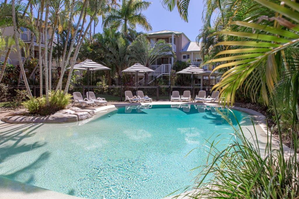 a swimming pool with chairs and umbrellas at Sandy Beach Resort in Noosaville