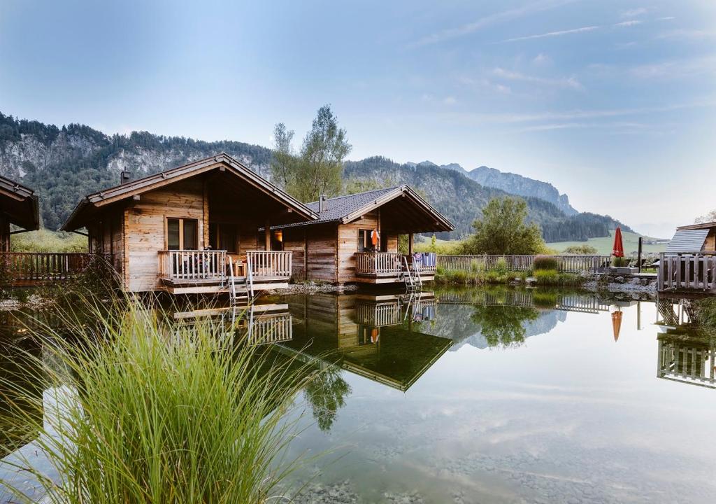 uma cabana de madeira num lago com montanhas ao fundo em Golf- und Sporthotel Moarhof em Walchsee