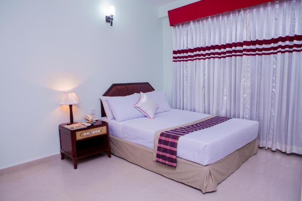 a bedroom with a bed and a table with a night stand at Meridian Hotel in Chittagong