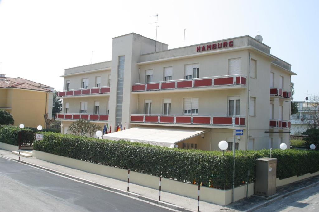 a large white building with red balconies on a street at Hotel Hamburg in Senigallia