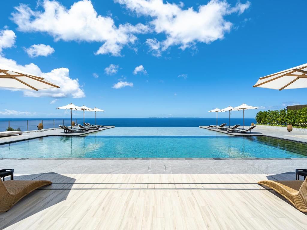 a pool with chairs and umbrellas and the ocean at One Suite THE GRAND in Nakijin