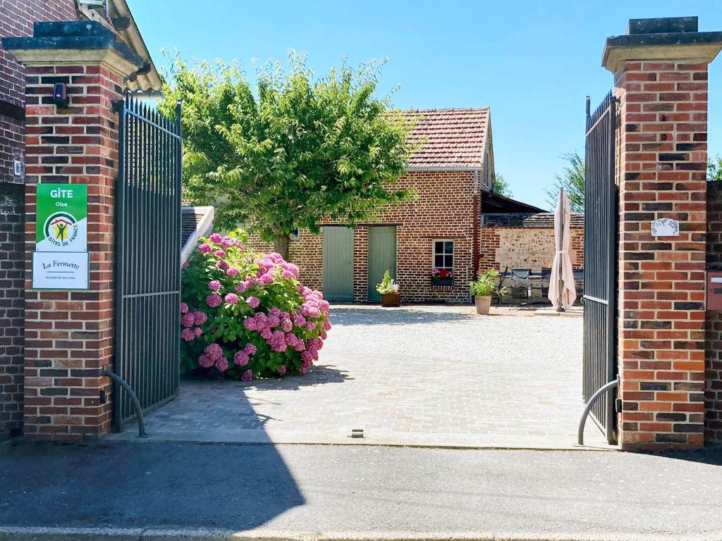 een poort naar een bakstenen gebouw met roze bloemen bij La Fermette in Andeville