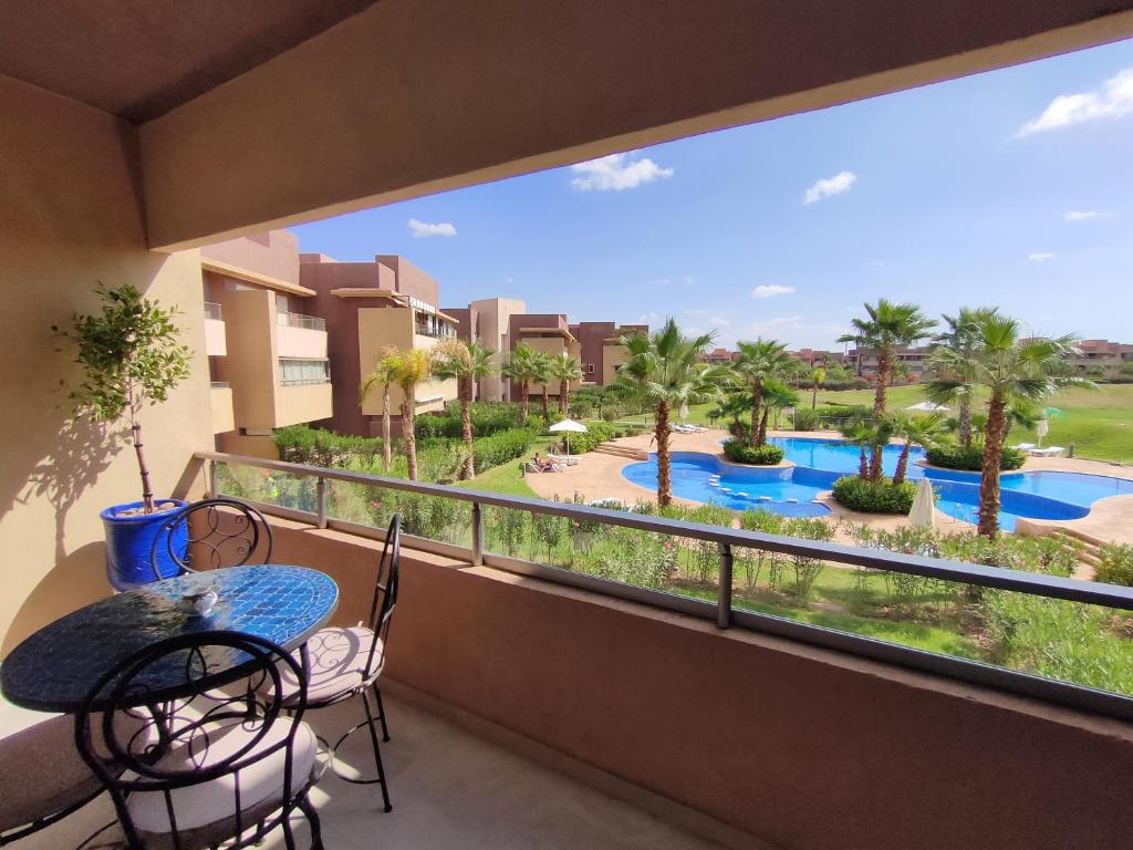 balcone con tavolo, sedie e vista sulla piscina di Prestigia Marrakech Golf 'Dar Cheryana' a Marrakech