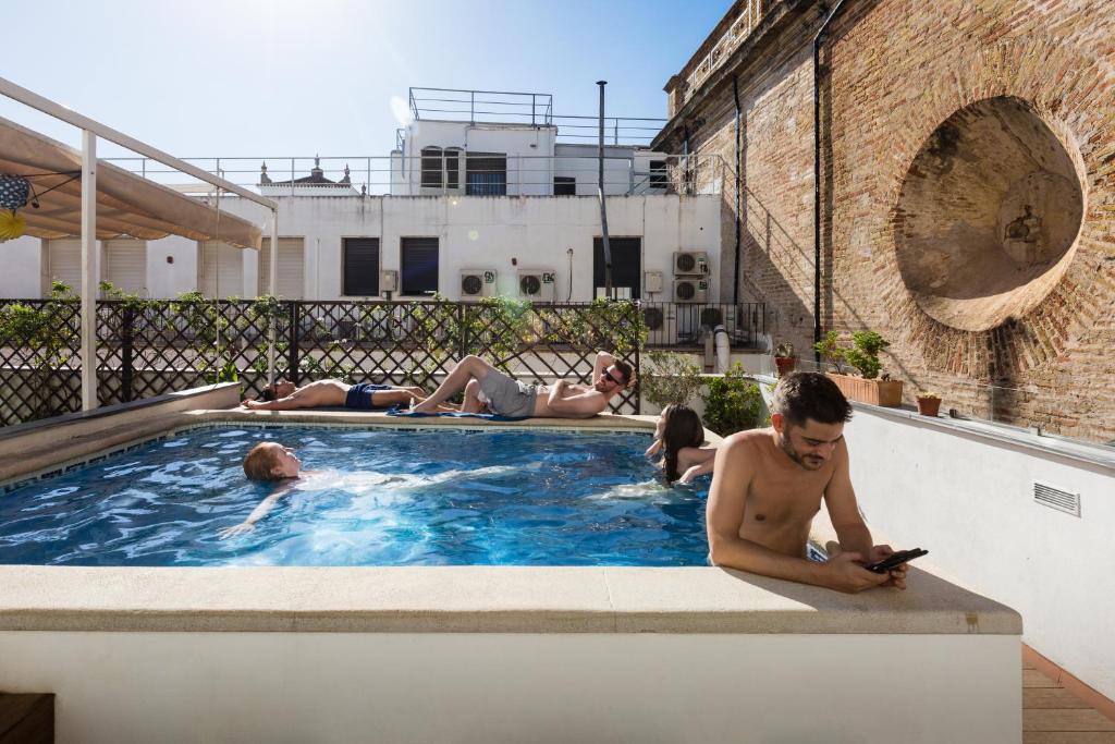 un homme dans une piscine en train de regarder un téléphone portable dans l'établissement Oasis Backpackers' Hostel Sevilla & Coworking, à Séville