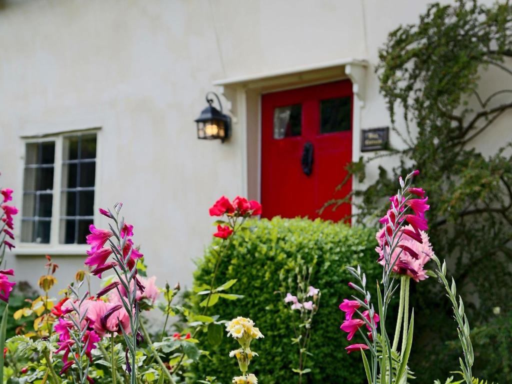 uma porta vermelha numa casa branca com flores em Box Cottage em Eastling
