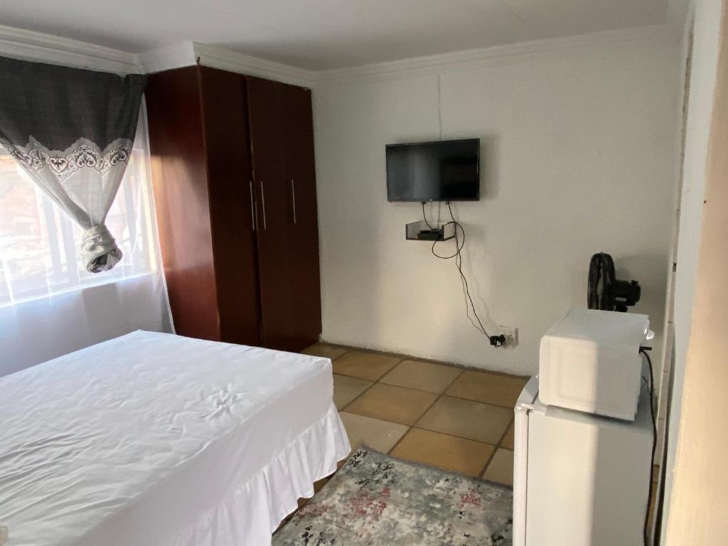 Soweto Towers Guest Accommodation في سويتو: غرفة نوم بسرير وتلفزيون وثلاجة