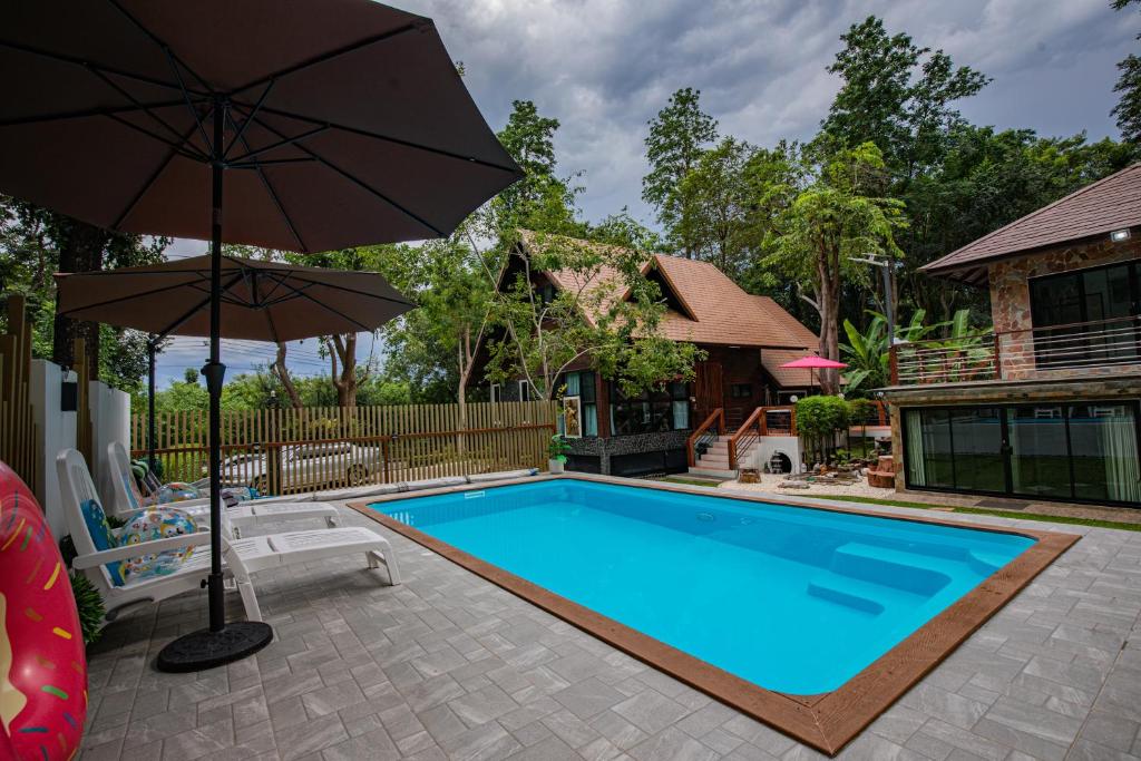 a swimming pool with an umbrella next to a house at Thanviman Forest Villa Kanjanaburi in Ban Tha Manao
