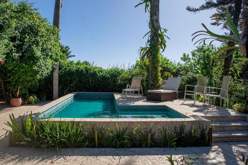 uma piscina num quintal com duas cadeiras e uma mesa em Casa até 34 hóspedes 200 metros da praia de Geribá com piscina e churrasqueira em Búzios