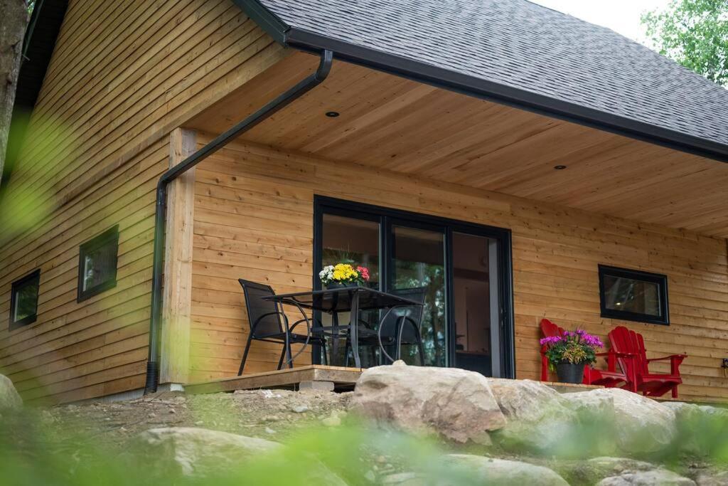 a house with a table and chairs on the porch at Private Off Grid Cottage Nestled in Nature With Waterfront in Barrys Bay