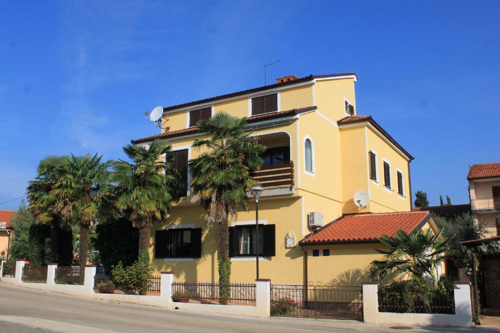 a yellow house with palm trees in front of it at Apartments by the sea Umag - 6095 in Umag