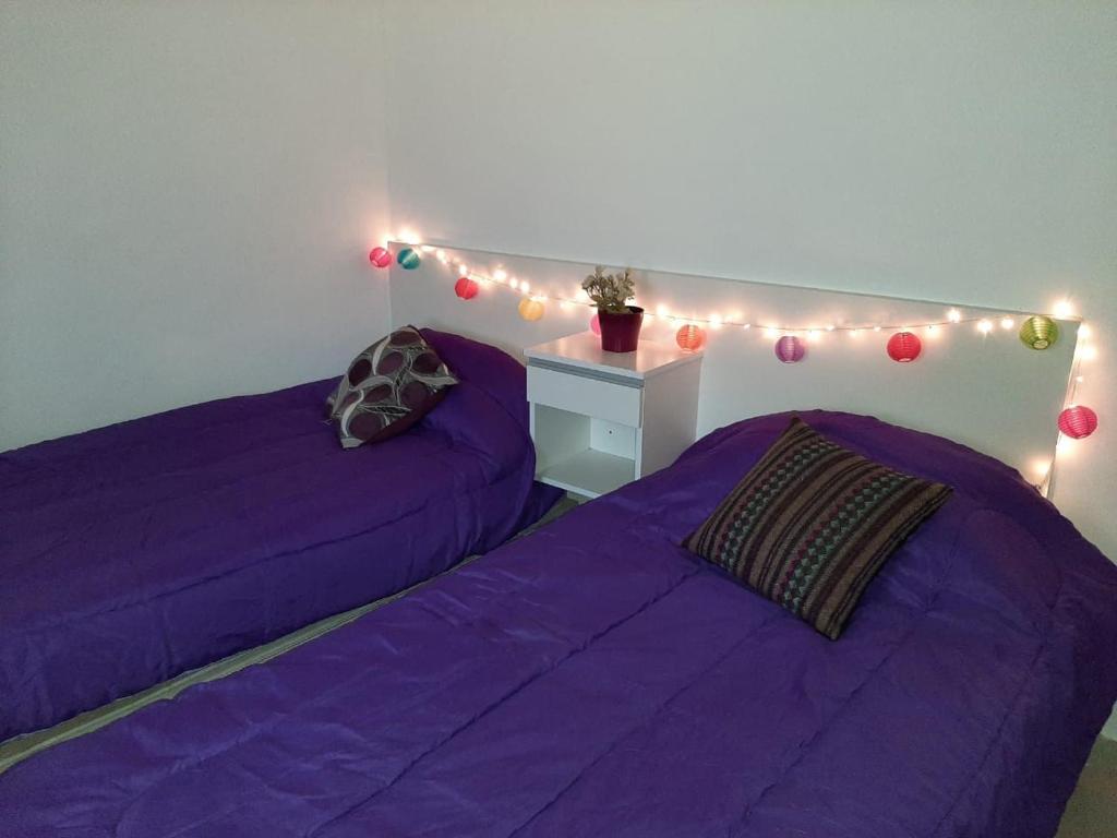 two beds in a room with purple sheets and lights at BenjaCha in Cerrillos