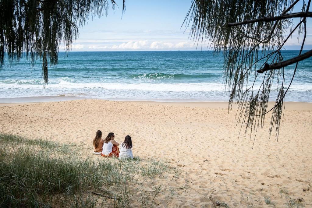 três raparigas sentadas na areia na praia em Coastal Getaway Across From Dicky Beach em Caloundra