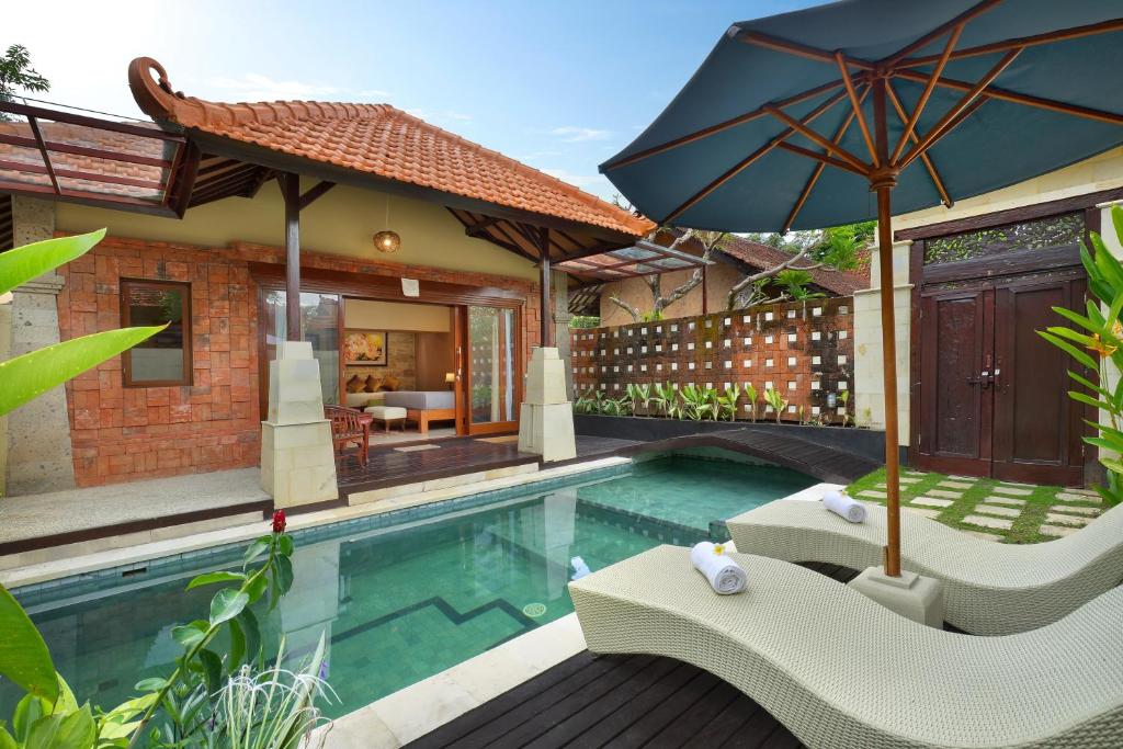 a swimming pool with two chairs and an umbrella at Mahe Garden Inn and Villas by Kamara in Kuta