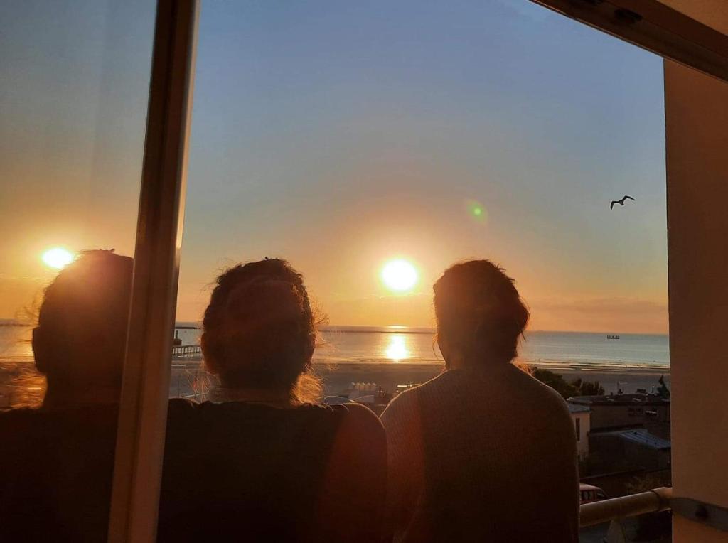 a group of three people looking out a window at the sunset at "BELLEVUE" Magnifique appartement vue sur mer et face à Nausicàa in Boulogne-sur-Mer