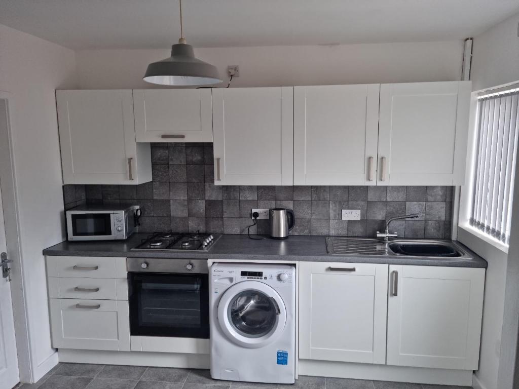 a kitchen with white cabinets and a washing machine at 3 bedroom house-Ellesmere Port in Ellesmere Port