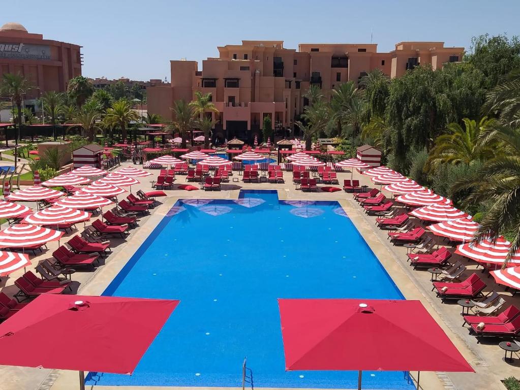 a resort pool with red and white umbrellas and chairs at Mövenpick Hotel Mansour Eddahbi Marrakech in Marrakesh