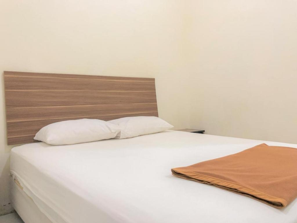 Cama blanca con cabecero de madera y almohadas blancas en Hotel Lido 88 Sorong Mitra RedDoorz en Sorong