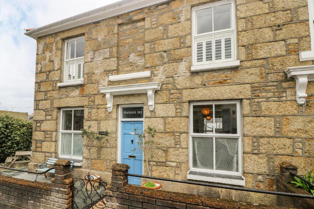 una casa de ladrillo con una puerta y ventanas azules en Mackerel Sky, en Penzance