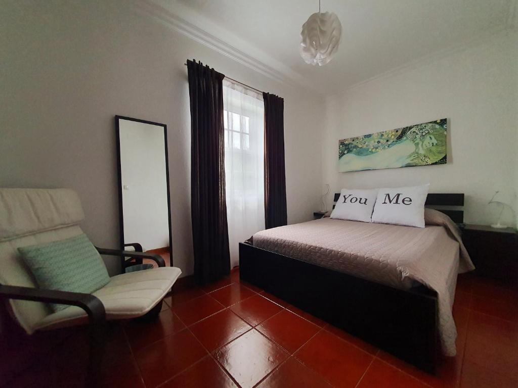 a bedroom with a bed and a chair and a mirror at Casa do Lado, Flores Açores in Lajes das Flores