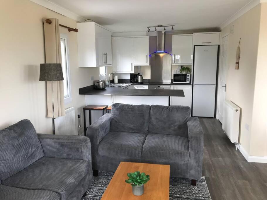 a living room with a couch and a table and a kitchen at Marios Lodge in Padstow