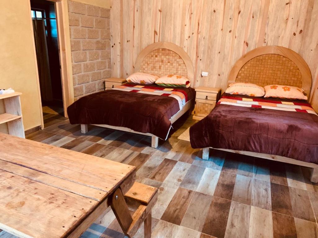 two beds in a room with wooden walls and wooden floors at Cabañas Zacatlan Zacapa in San José Ayotla