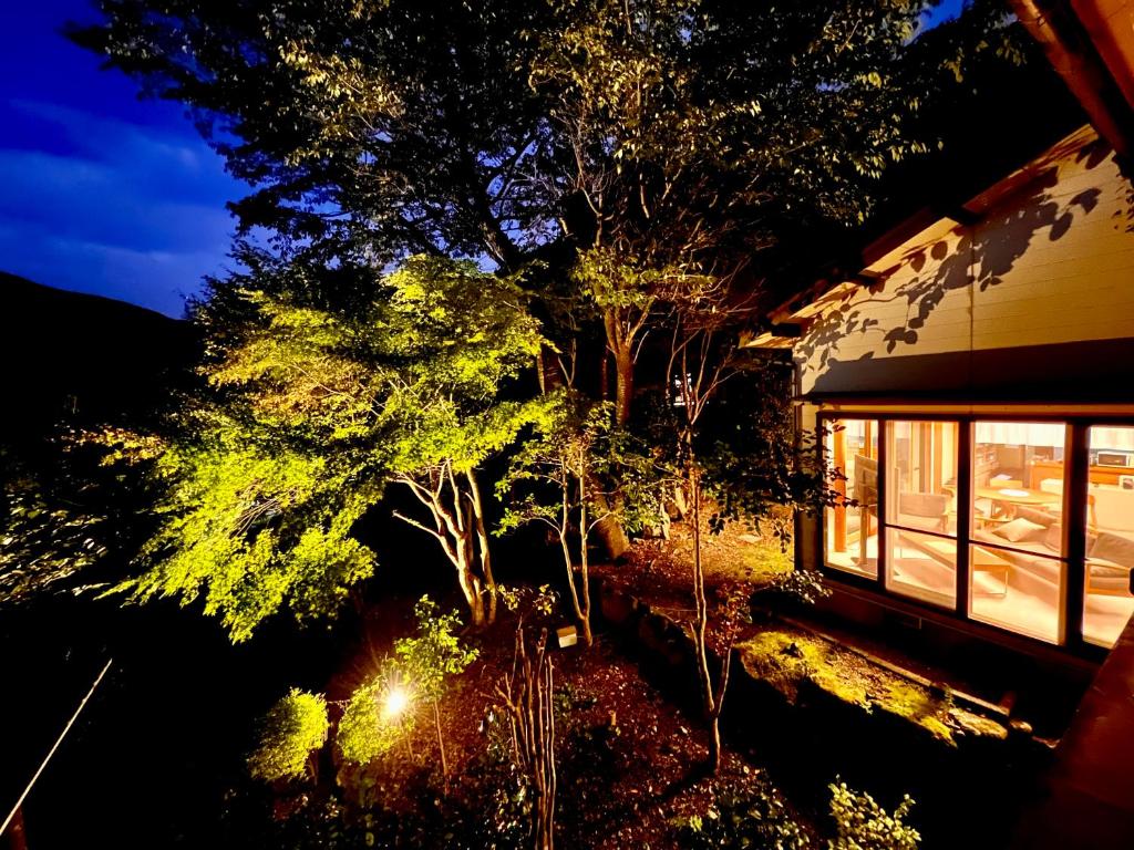 una vista nocturna de una casa con árboles al lado en 湯布院 星の里 Yufuin Hoshinosato en Yufu