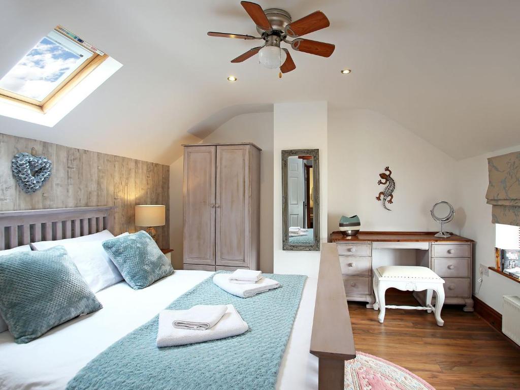 a bedroom with a bed with a ceiling fan and a desk at 2 West Cottage in Blakeney