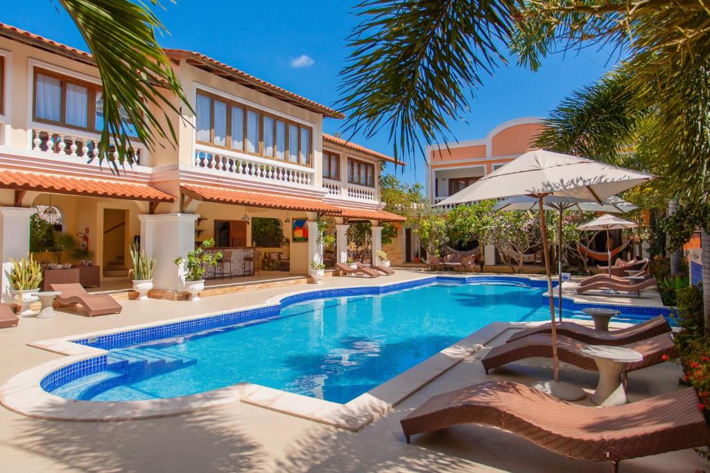 a villa with a swimming pool with chairs and an umbrella at Hotel Villa Beija Flor in Jericoacoara