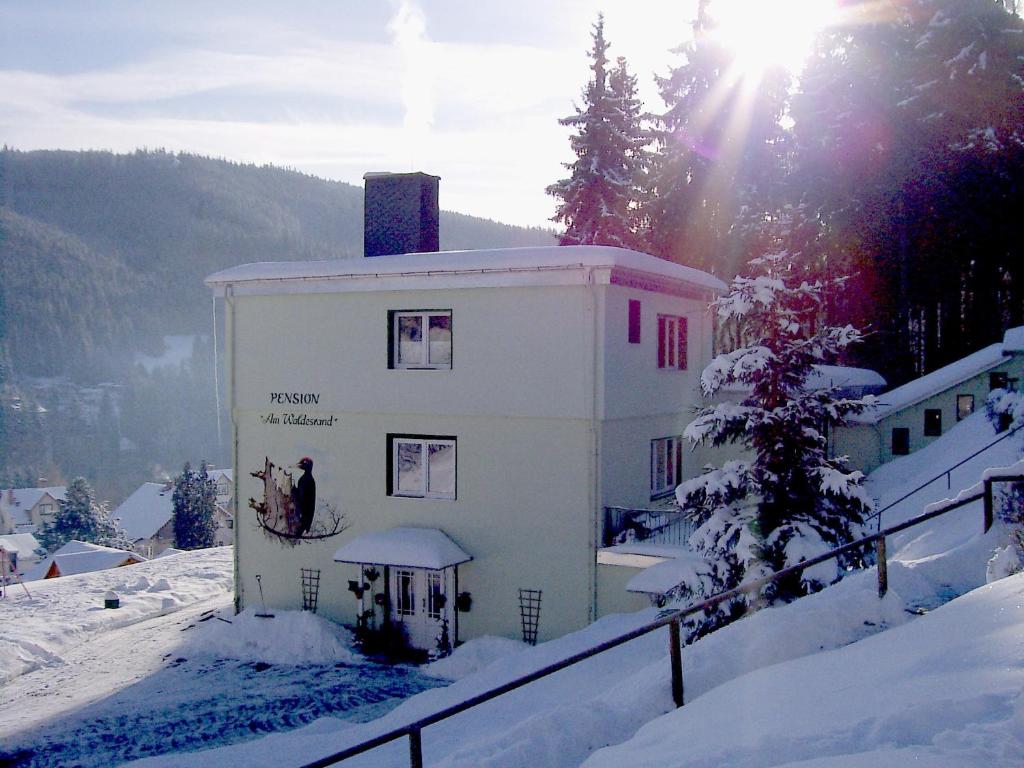 a building in the snow with the sun behind it at Pension Am Waldesrand in Ilmenau