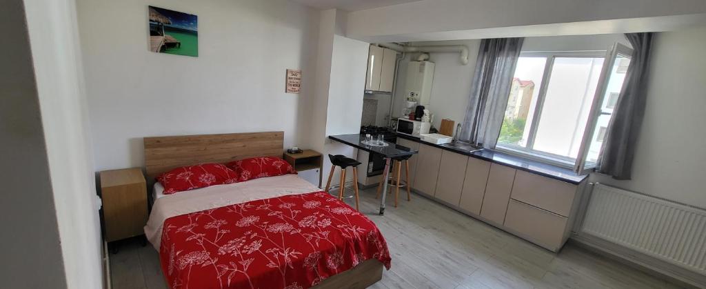 a bedroom with a bed with red sheets and a kitchen at Self check-in Studio 22 Bulevardul Oltenia in Craiova