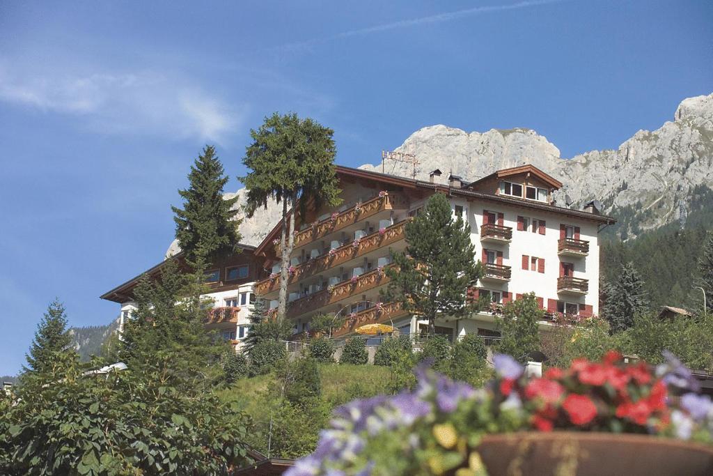 a building on a hill with mountains in the background at Hotel Catinaccio Rosengarten in Moena