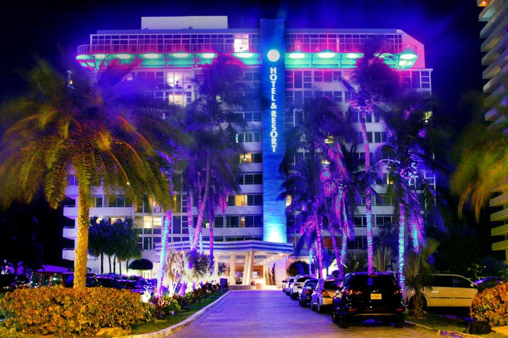 a building with palm trees in front of it at night at Ocean Manor Beach Resort in Fort Lauderdale