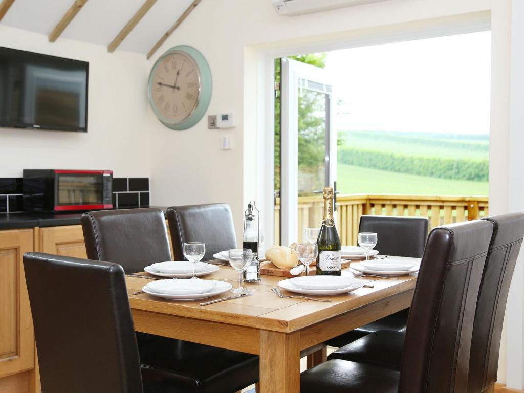 a dining room table with chairs and a clock on the wall at Kentish Barn Retreat in Chilham