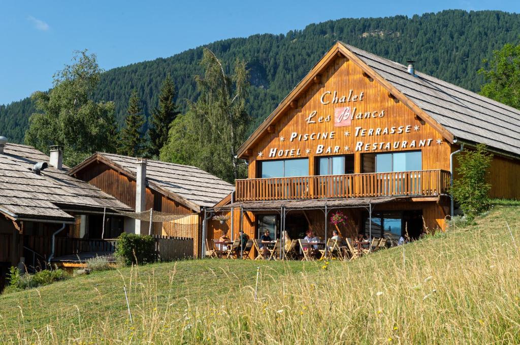 a large wooden building with people sitting outside of it at Chalet Hôtel Les Blancs in Pra-Loup