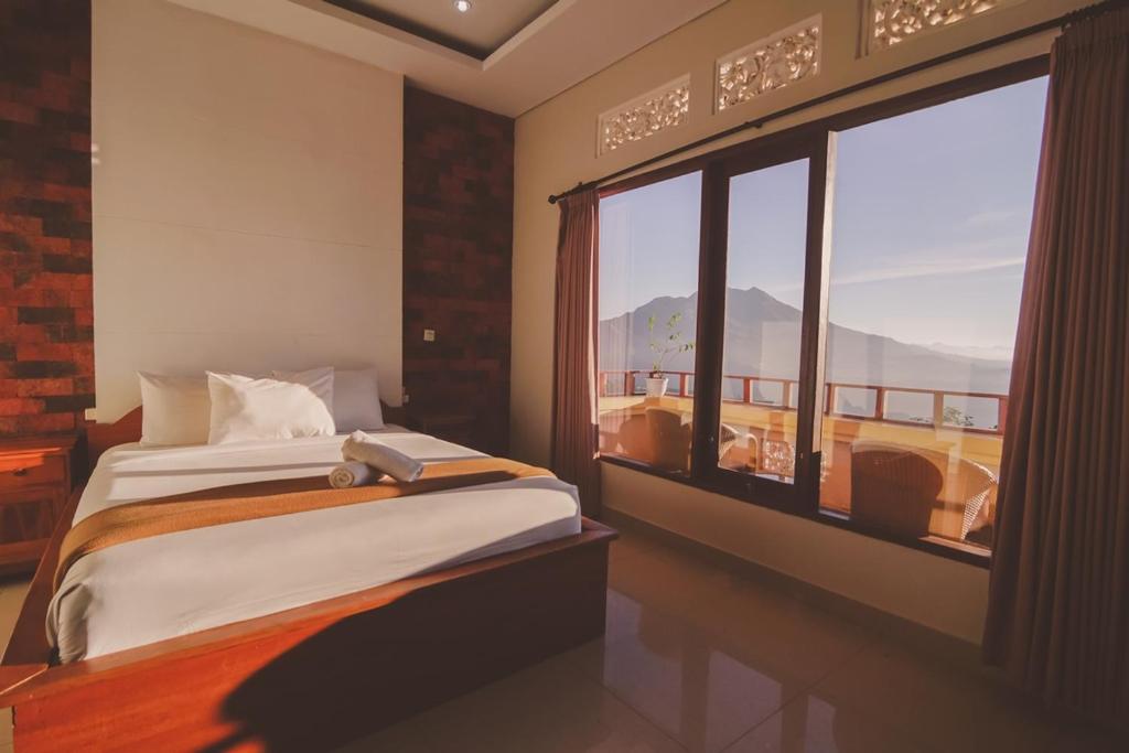 a bedroom with a bed and a large window at caldera hotel in Kintamani