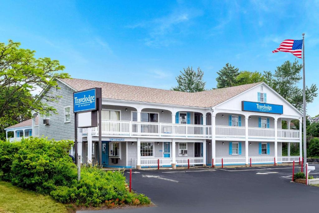 a large white inn with an american flag at Travelodge by Wyndham Cape Cod Area in West Dennis