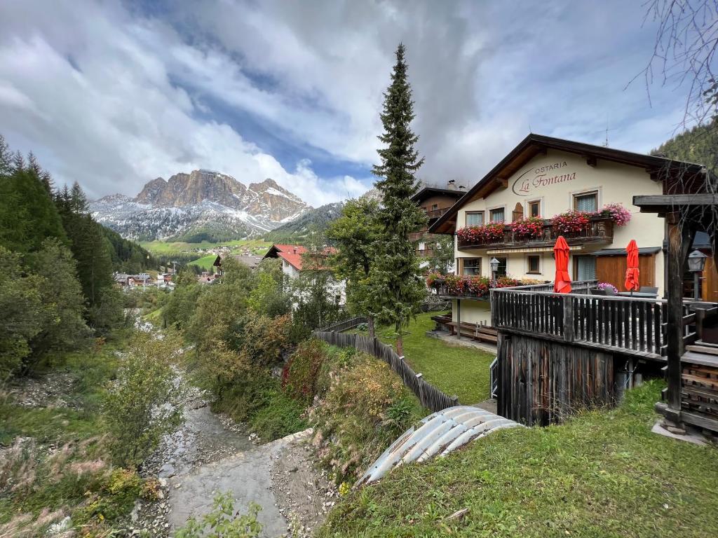 a building on a hill with a river and mountains at Ostaria La Fontana in Corvara in Badia