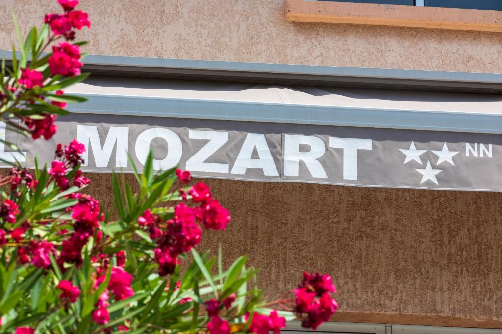 een bord aan de zijkant van een gebouw met roze bloemen bij Hôtel Le Mozart in Aix-en-Provence