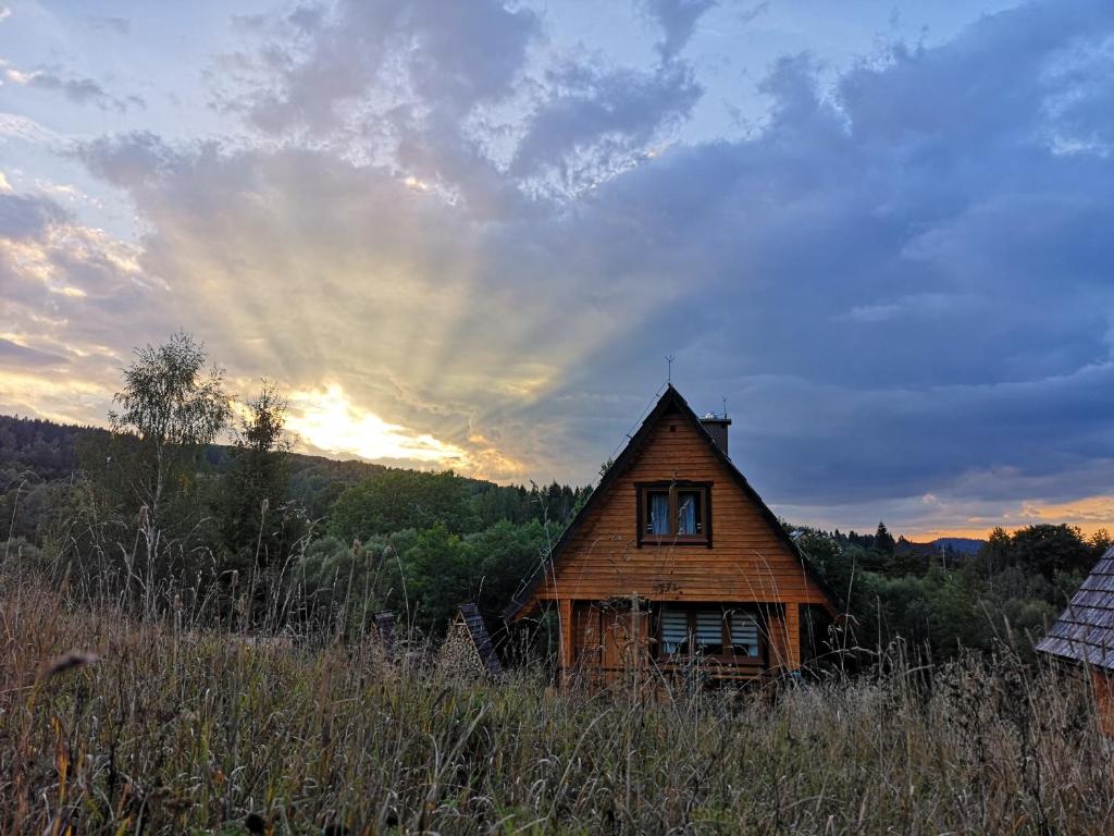 an old house sitting in a field with the sun setting at Domki Obertyny in Wetlina