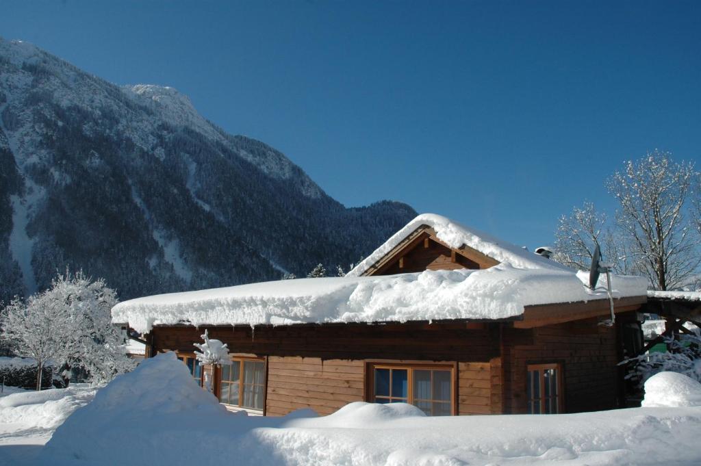 ein von Schnee bedecktes Blockhaus mit Bergen im Hintergrund in der Unterkunft Haus Masonblick in Braz