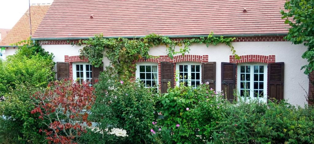 uma casa branca com um telhado vermelho e alguns arbustos em Chantilly ,petit déjeuner et table d'hôtes possible em Noyers