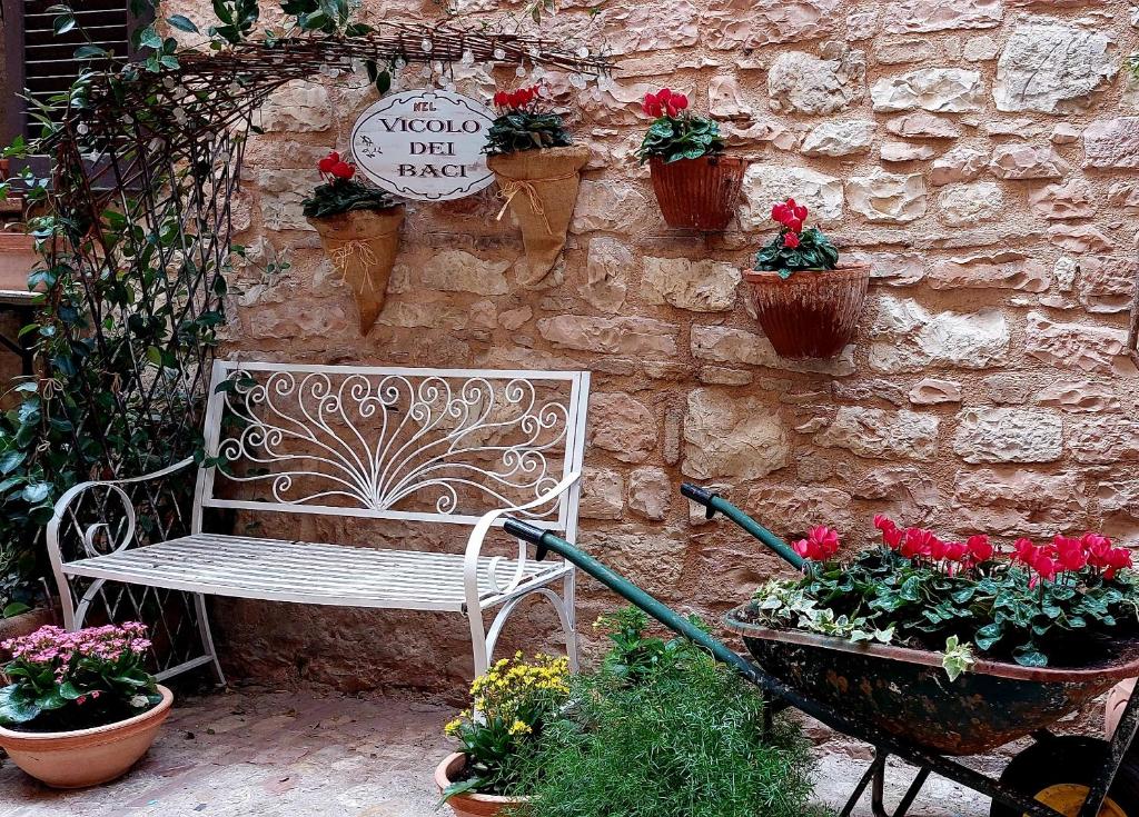 un banco blanco sentado junto a una pared de piedra con macetas en Nel vicolo dei Baci - Casa vacanze al Bacio, en Spello